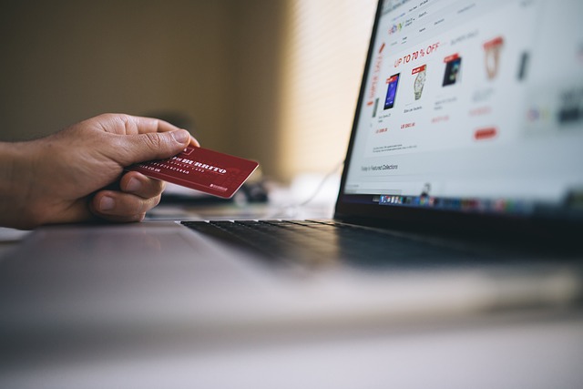 Opened laptop. an online store can be seen blurred on the screen. in front of it a hand with a credit card